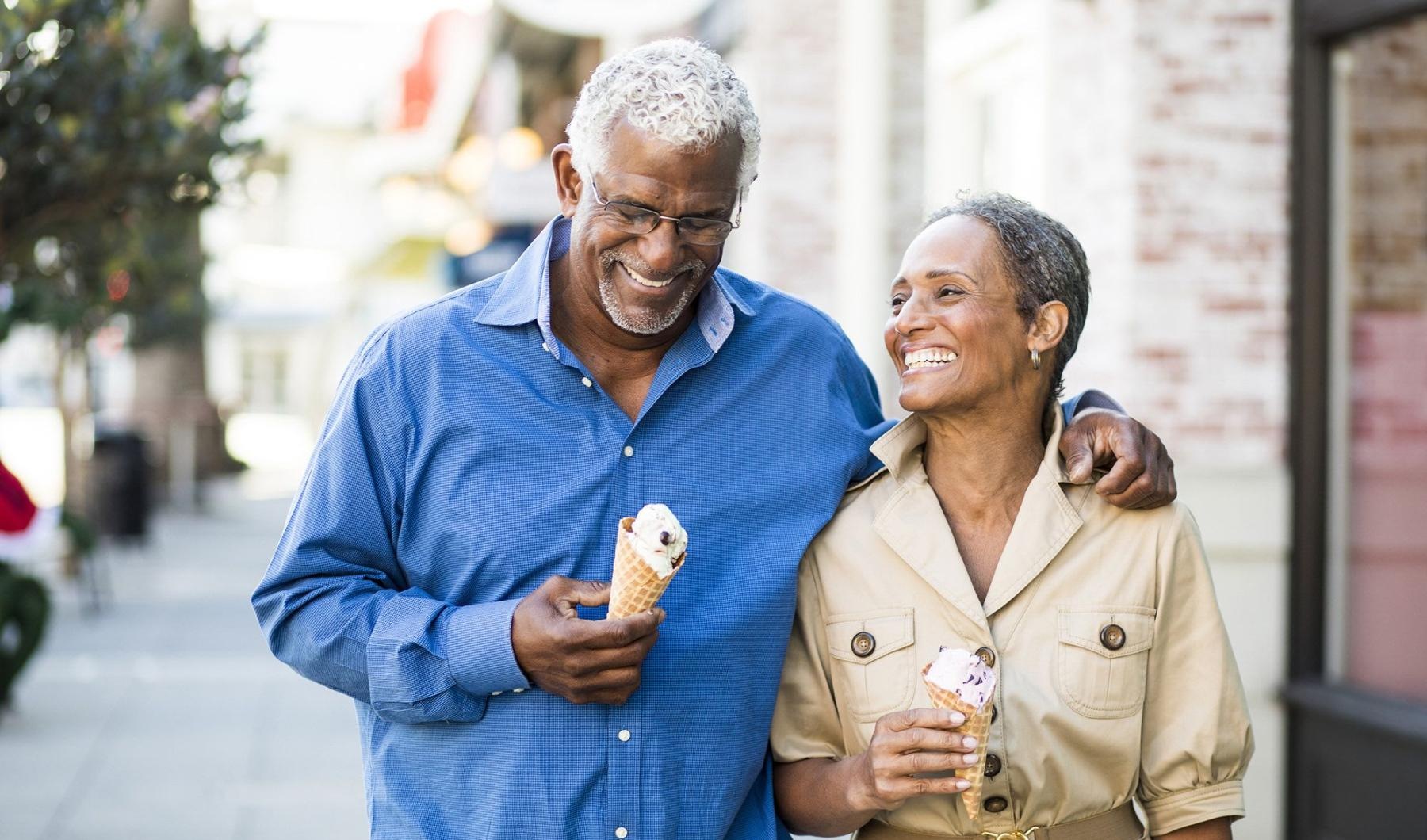 older couple walks down city sidewalk while holding ice cream cones